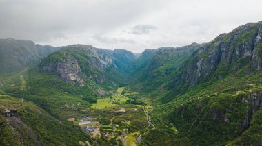 Dik uçurumlar, yemyeşil vadiler, dolambaçlı yollar, dağınık binalar ve bulutlu bir gökyüzü içeren Lysebotn, Norveç 'in hava manzarası..