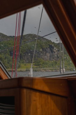 Tahta yelkenli iskeleti, halatlar ve sakin bir Norveç fiyordunda sakin sular boyunca yemyeşil bir yamaç..