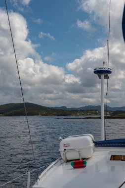 NXT radarlı bir yelkenlinin pruvası ve güvertede bir cankurtaran salı Norveç 'te yeşil tepeler ve dağınık binalarla sakin bir fiyortta geziniyor..