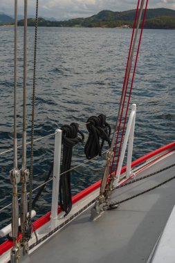 Yelkenlinin güvertesinde, yeşil tepeler ve uzak dağlarla çevrili sakin mavi sularda yüzen siyah halatlar ve kırmızı halatlar vardı..