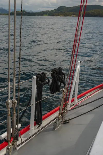 Yelkenlinin güvertesinde, yeşil tepeler ve uzak dağlarla çevrili sakin mavi sularda yüzen siyah halatlar ve kırmızı halatlar vardı..
