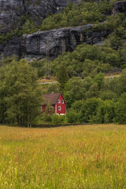Uçsuz bucaksız çatılı canlı kırmızı bir ev, Norveç 'in Lysebotn kentindeki sarp kayalıkları ve soluk elektrik hatları olan yeşilliklerle çevrili bir çayırda oturuyor..