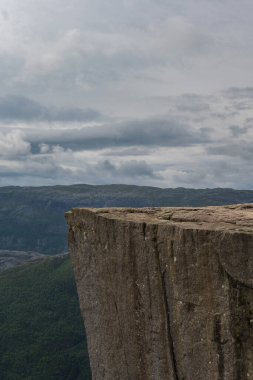 Norveç 'teki ikonik Preikestolen uçurumu düz, dikey bir düşüş, yemyeşil ormanlar, engebeli arazi ve bulutlu bir gökyüzü içerir..