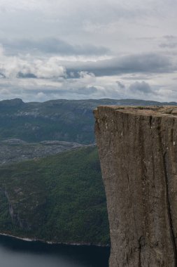 Norveç 'teki Lysefjord' un üzerindeki düz uçurum yeşil tepeler, engebeli dağlar ve bulutlu gökyüzünün altındaki karanlık fiyortlarla çevrilidir..