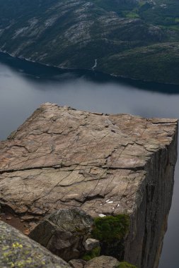 Norveç 'teki Lysefjord' un üzerinde kayalık bir zemin, dik damlalar, dingin fiyort suları ve çağlayan uzak bir şelale bulunur..