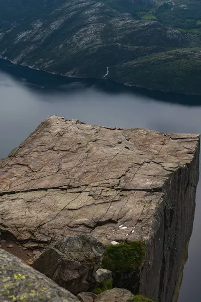 Norveç 'teki Lysefjord' un üzerinde kayalık bir zemin, dik damlalar, dingin fiyort suları ve çağlayan uzak bir şelale bulunur..