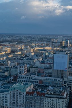 Varşova, Polonya 'nın yüksek manzarası, tarihi ve modern mimari sergileniyor, renkli çatılar, ve şehir manzarası üzerinde parçalı bulutlu bir gökyüzü.