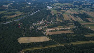 Polonya 'nın Nowy Lubiel kenti yakınlarındaki kırsal bir köyün hava görüntüsü, dağınık evler, sık ormanlar, tarımsal alanlar ve kıvrımlı bir nehir.