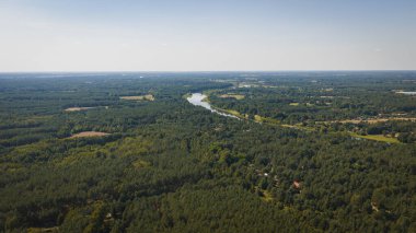 İnsansız hava aracı, Polonya 'nın Nowy Lubiel kenti yakınlarındaki bereketli bir ormanı, dalgalı bir nehri, dağınık berraklıkları, küçük binaları ve ufukta açık mavi gökyüzünü yakalar..