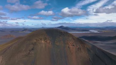 İnsansız hava aracı İzlanda 'da volkanik bir krater sırtının üzerinden geçiyor. Bu dağ yürüyüşçülerini, dolambaçlı bir nehri, dağınık gölleri ve arka planda engebeli volkanik ovaları gösteriyor..