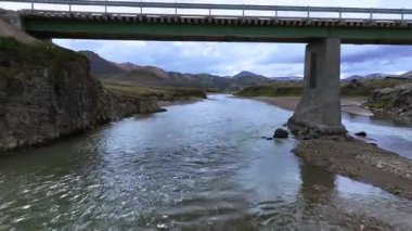 Dönen bir nehrin havadan görünüşü çorak, kayalık bir ovayı kesiyor. Yuvarlanan tepeler, uzak dağlar ve parçalı bulutlu bir gökyüzü..