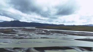 Drone, İzlanda 'da örülmüş bir nehir sistemini süpürüyor. Karmaşık su desenlerini, engebeli karlı dağları ve bulutlu gökyüzünü ortaya çıkarıyor..