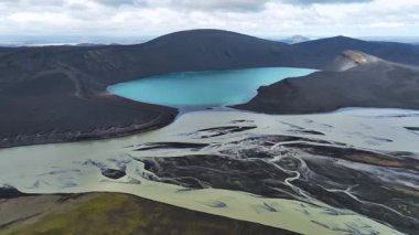 Karanlık volkanik araziyle çevrili, dalgalı mavi krater gölü, engebeli İzlanda manzarası boyunca akan örülmüş nehirler..