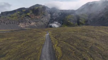İnsansız hava aracı engebeli uçurumlar, çakıllı bir yol, volkanik kayaları kaplayan yosun ve İzlanda 'daki çorak bir arazide yükselir..
