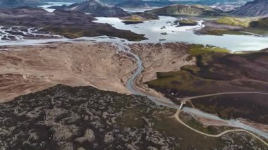 İzlanda 'da örülmüş bir nehir sisteminin hava görüntüsü. Köprü, volkanik arazi, kumlu nehir kıyıları ve çevresindeki toprak yollarla çelişiyor..