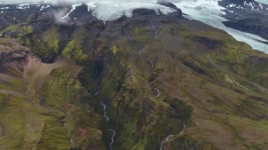 İnsansız hava aracı İzlanda 'da bir buzulun üzerinde ileri geri hareket eder, buzla kaplı araziyi, yosun kaplı dağları, çağlayan nehirleri ve alçak asılı bulutları ortaya çıkarır..
