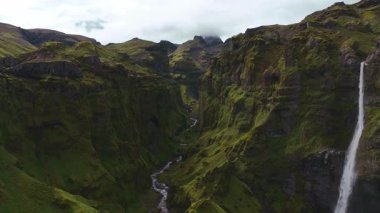 İnsansız hava aracı, İzlanda 'nın engebeli manzaralarıyla çevrili yosun kaplı uçurumları olan yemyeşil bir kanyonda çağlayan yüksek bir şelaleye yaklaşıyor..