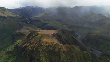 İnsansız hava aracı sarp yeşil uçurumları ve dolambaçlı bir nehirle derin kanyonları süpürüyor. Sis ve bulutlarla kaplı kar örtülü dağları ortaya çıkarıyor..