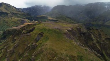 İnsansız hava aracı sarp kayalıkların ve derin kanyonların üzerinden geçer aşağıdaki dolambaçlı nehir yemyeşil araziyi, açıkta kalan kayaları ve sisli bulutlu gökyüzünü gözler önüne serer..