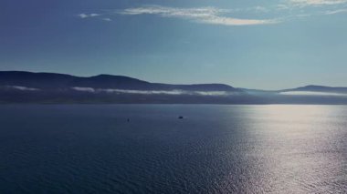 İzlanda 'da bir fiyort ya da körfezin sakin sularda, uzak dağlarda ve bulutların altında berrak bir gökyüzünün altında hareket eden bir tekne..