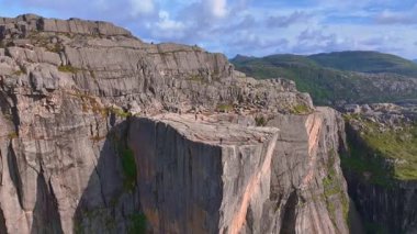 Drone Preikestolen 'in düz uçurumunu yakalar, Lysefjord' a dik bir düşüş, yemyeşil dağlar ve açık mavi gökyüzü altında ziyaretçiler.