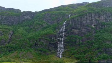 Norveç 'in Lysebotn şehrinde yemyeşil yemyeşil bir kayalıklardan dökülen yüksek bir şelalenin havadan görünüşü. Su dinamik bir şekilde karanlık kayaya doğru akar..