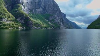Lysebotn 'da bir fiyortta süzülen pürüzsüz bir dron kayalık uçurumları, küçük bir şelaleyi, sakin suyu ve bulutlu bir gökyüzünün altındaki uzak dağları gösteriyor..