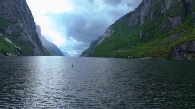 Norveç 'in Lysebotn yakınlarındaki koyu yeşil fiyortta, yemyeşil uçurumlar ve arka planda çağlayan bir şelale ile sorunsuzca ilerleyen bir kanocu..