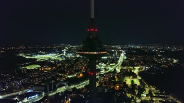 Litvanya 'daki Vilnius TV Kulesi' nin gece görüşü, ışıklı gözlem güvertesi ve parıldayan şehir manzarası. Kamera kulenin etrafında sorunsuzca hareket ediyor..