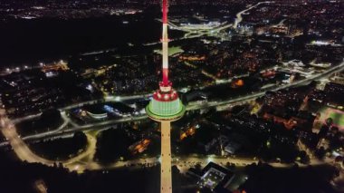 Litvanya 'daki Vilnius TV Kulesi geceleri kırmızı, beyaz ve yeşil parlar. Hava görüntüsü yüksekliğini, silindirik yapısını ve kentsel çevresini gösterir..