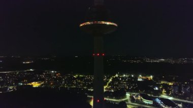 Vilnius TV Kulesi gece kırmızı ışıklarla parlıyor, gözlem güvertesi görünür. Kamera hareket ediyor, kuleyi ve şehrin ışıklarını yakalıyor..