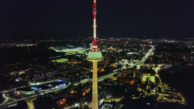 Vilnius TV Kulesi geceleri canlı bir şehirle çevrili kırmızı ve beyaz ışıklarla parıldıyor. Hava hareketi yüksekliğini ve kentsel ayarlarını vurgular.