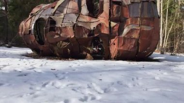 Bir dron karlı bir ormanın üzerinden yükselir, uzun ağaçları, çalılıkları ve paslı bir helikopter gövdesini gözler önüne serer..