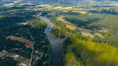 Polonya 'nın Nowy Lubiel şehrinde kıvrılan bir nehrin hava manzarası, yeşil alanlar, ormanlar, dağınık evler ve kasabayı birbirine bağlayan uzak bir köprü..