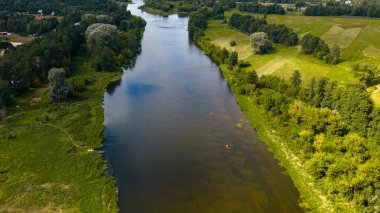 Polonya 'nın Nowy Lubiel şehrinde iki kano, yeşil tarla, sık ormanlar, dağınık binalar ve yansıtıcı berrak su bulunan bir nehrin havadan görünüşü.