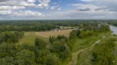 Polonya 'nın Nowy Lubiel şehrinden yeşil ve ormanla çevrili dolambaçlı bir nehir akar. Kırmızı çatılı ev de dahil olmak üzere tarlalar ve bir grup bina görülebilir durumda..