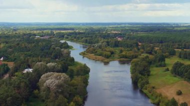 Polonya 'nın Nowy Lubiel kentindeki orman ve tarlalardan akan bir nehrin havadan görünüşü, dağınık binalar görünür ve nazik insansız hava aracı hareketleriyle.