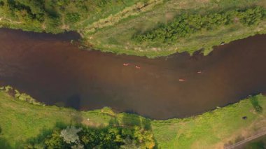 Polonya 'nın Nowy Lubiel kentindeki yeşil tarlalar ve bitkiler arasında süzülen bir nehrin havadan görünüşü. Kano sahipleri kürek çekiyor ve suda dalgalanmalar yaratıyor..