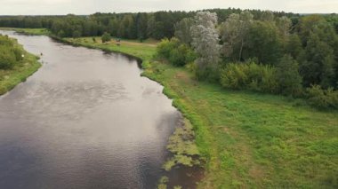 Polonya 'nın Nowy Lubiel kentinden akan bir nehrin havadan görünüşü. Çimenli bankalar, yoğun ağaçlar ve deniz kenarında sakin bir ortamda oturan bireyler..