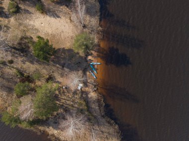 Bitmeyen yeşil ve yaprak döken ağaçlar, kumlu bir sahil, mavi kanolar ve karanlık bir göl veya nehrin yakınındaki insanların hava görüntüsü..