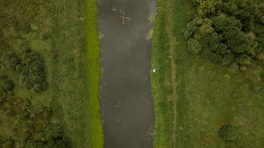 Berezivka, Minsk, Belarus yakınlarındaki yemyeşil, ağaçlar ve çalılarla çevrili dar bir nehrin havadan görünüşü, sağ kıyıda küçük beyaz bir nesne ile.