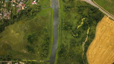 Beyaz Rusya 'nın Minsk kentinde yaz aylarında çimenleri bölen bir nehrin, küçük bir yerleşim yeri, sık ağaçlar ve hasat edilen bir tarlanın havadan görünüşü..
