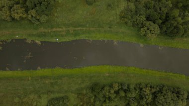 Yeşil çimenler ve sık ormanlarla çevrili dar bir nehir. Kıyıda beyaz bir nesne var. Yazın Berezivka ya da Minsk, Belarus yakınlarında yakalandı..