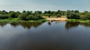 Beyaz Rusya 'da geniş bir nehir yoğun yeşilliklerden sakince akar. Küçük bir tekne kumlu bir nehir kıyısına doğru hareket eder ve suda dalgalanmalar yaratır..