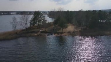 Beyaz Rusya 'da, sık ağaçlar ve küçük yarımadalarla çevrili sakin bir göl manzarası. İHA sorunsuz hareket ederken güneş ışığı suda parıldıyor..