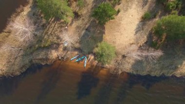 Beyaz Rusya 'da sakin sularla çevrili küçük bir yarımadanın havadan görünüşü, yeşil ağaçlar, çıplak dallar ve kıyı boyunca görünen kanolarla çevrili..