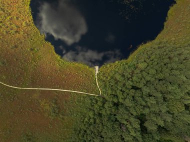 Bereketli yeşillikler, açık otlaklar ve Litvanya 'da dolambaçlı bir yol ile çevrili, yansıtıcı suya uzanan ahşap bir iskelenin hava görüntüsü..