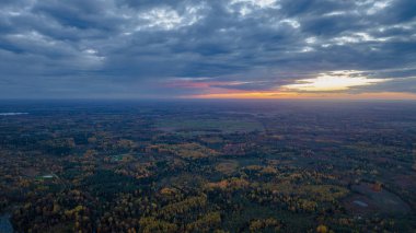 Günbatımında Litvanya manzarası, sonbahar ormanları, açık alanlar, küçük bir su kütlesi ve dramatik bulutlu bir gökyüzü..