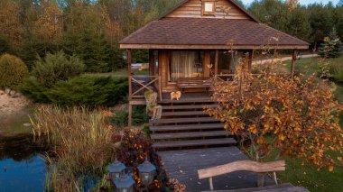 Verandası ve güvertesi olan ahşap bir kulübe, sazlıklar ve yansımalarla dolu sakin bir göletin yanındaki sonbahar ağaçlarının arasında oturur ve Litvanya 'da huzurlu bir doğal ortam yaratır..