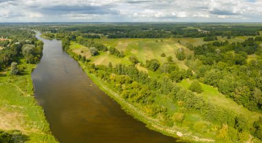 Polonya 'nın Nowy Lubiel kentindeki çimenli tarlaların ve sık ağaçların arasından süzülen dingin bir nehir, parçalı bulutlu bir gökyüzünün altında tarım arazileri ve ormanlarla doludur..